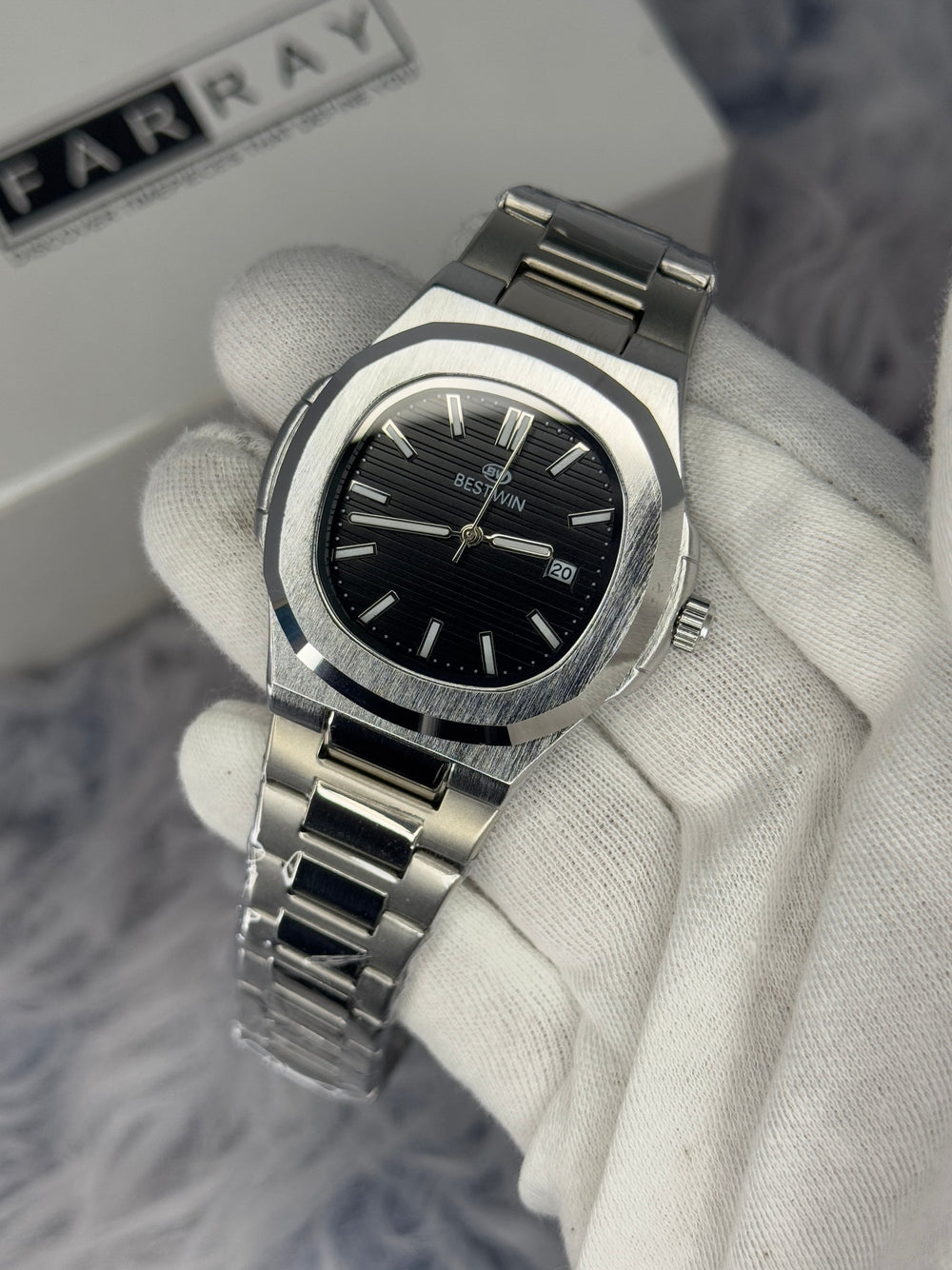 Silver watch with black face held by a gloved hand on a blurred background